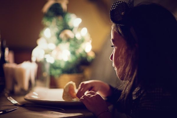Lonely and sad little girl is eating alone in the Christmas night. The film noise is added to the image.
