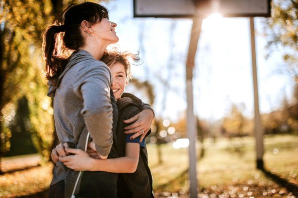 Beautiful mother hugging her son on basketball field on sunny autumn day