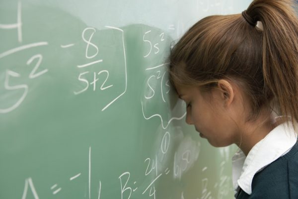 Teenage girl (12-14) resting head against math equation on chalkboard